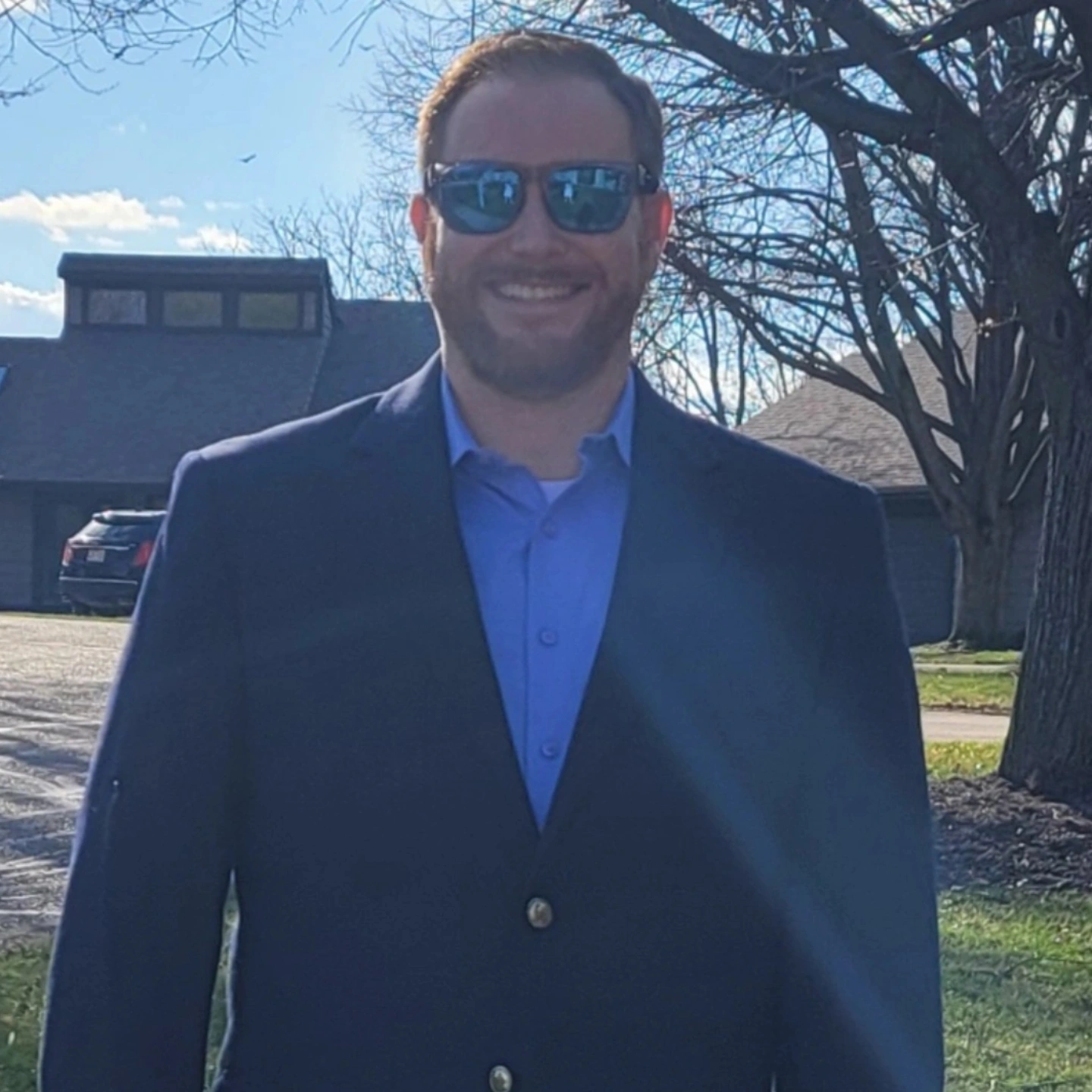 Paul Gover standing outdoors in a dark blue suit, blue shirt, and sunglasses
