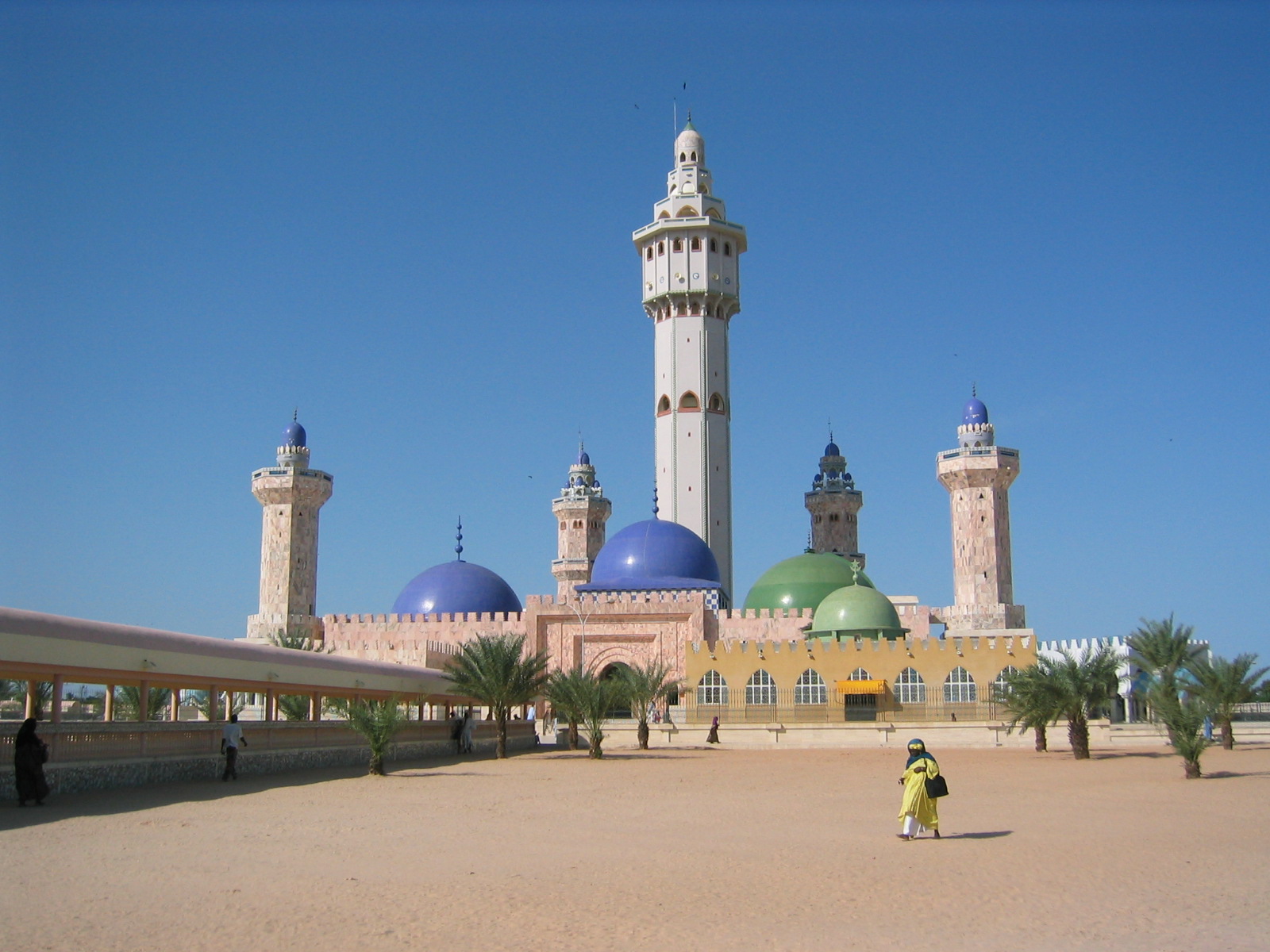 A mosque with domes and a tall minaret beneath a bright blue sky.