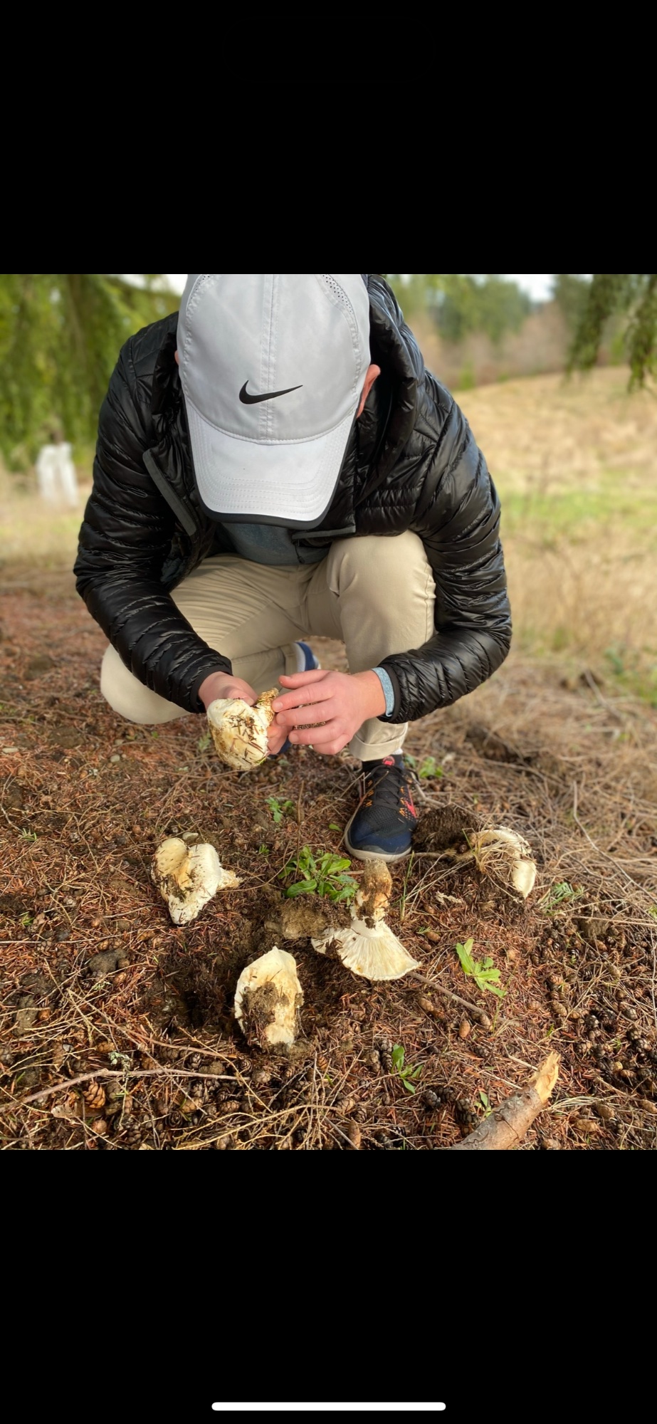 A person in a light cap crouches outdoors while examining an item in their hands
