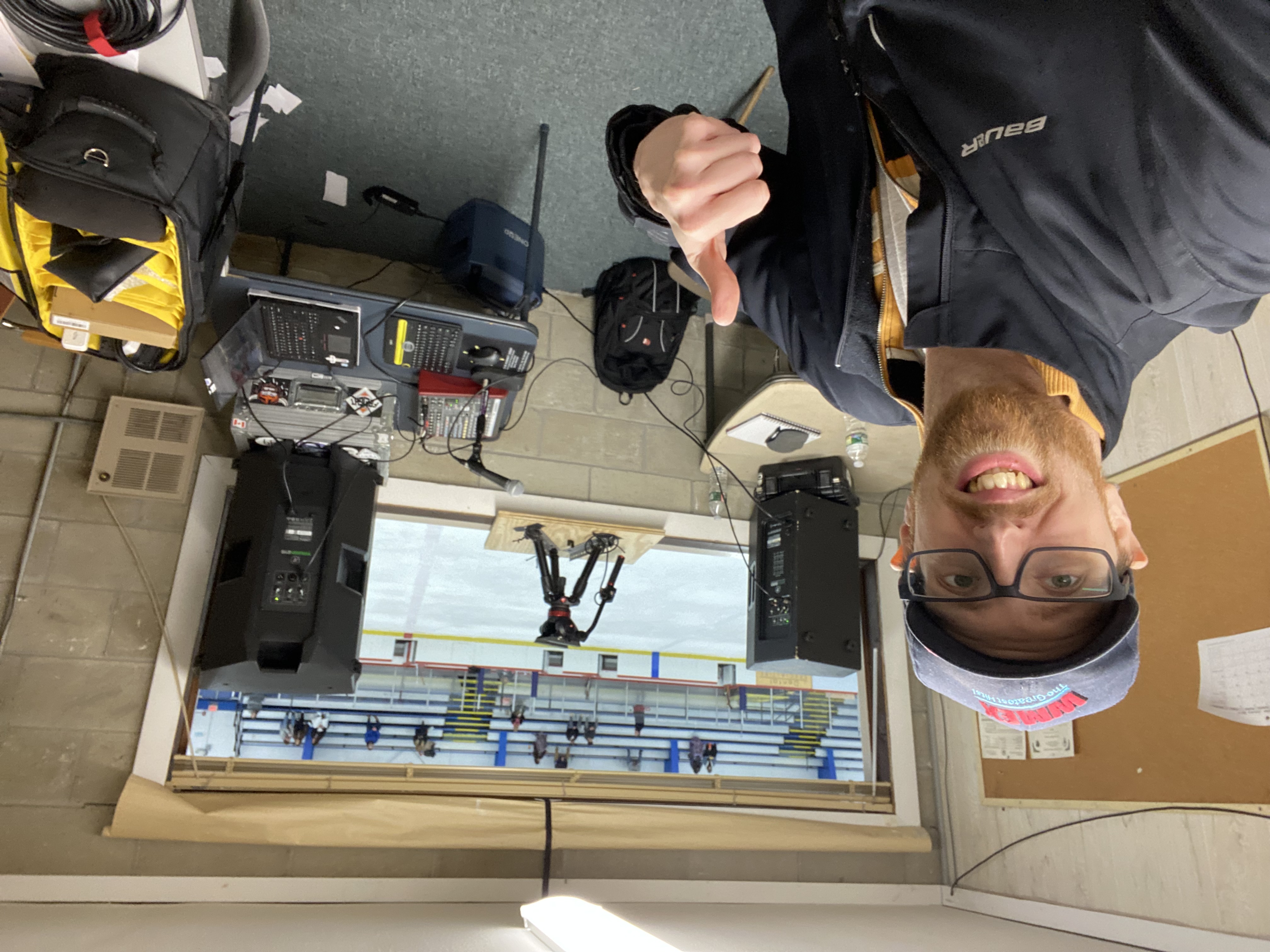 A rinkside audio booth with speakers, a mixing console, and the ice visible through the rink window.