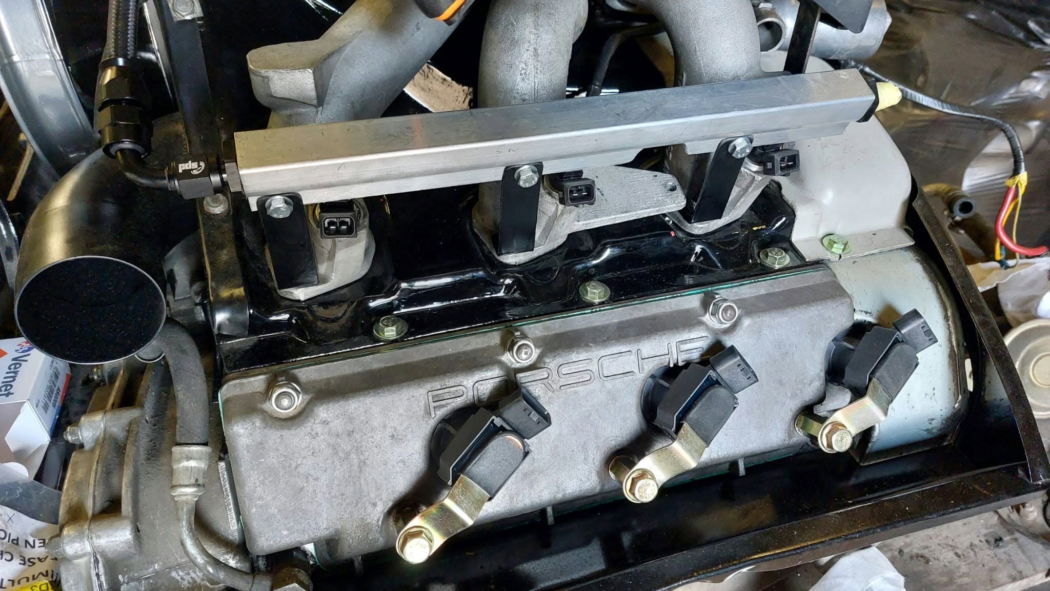 Close view of a Porsche engine with a metal fuel rail and ignition coils.