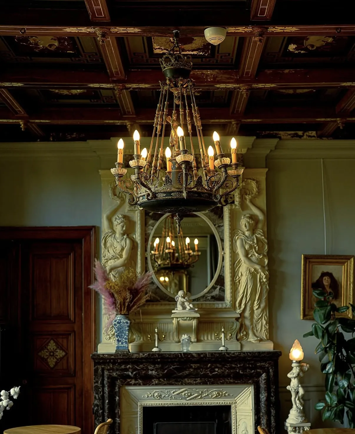 Lustre à bougies sous le plafond à caissons, cheminée de marbre et miroir encadré de cariatides