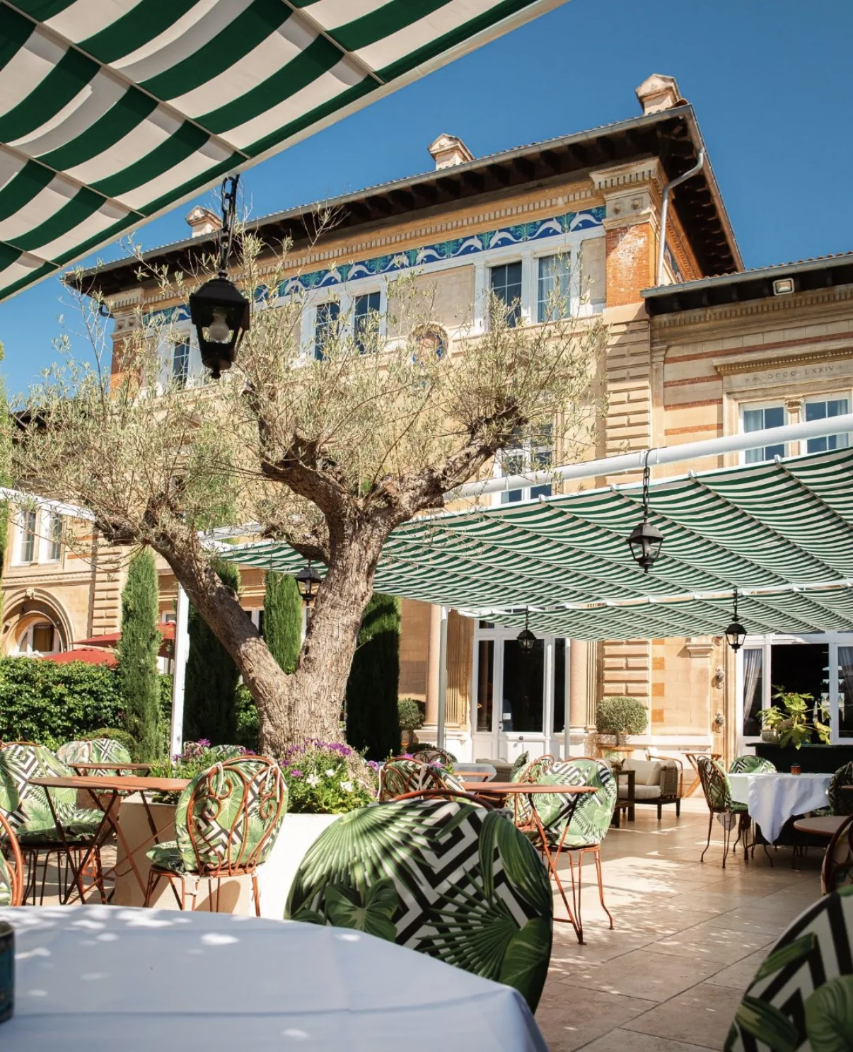 La façade du Château Beaupin et sa terrasse sous les stores rayés, vue depuis le jardin
