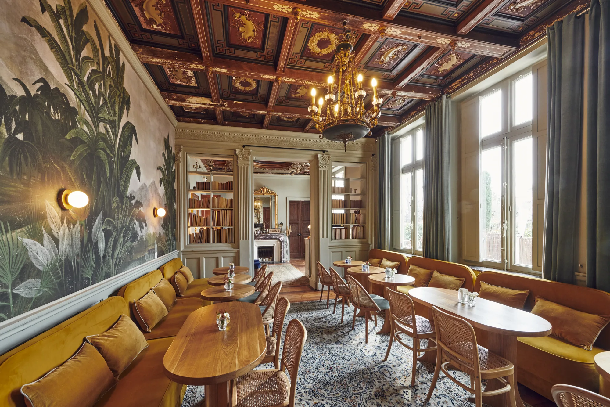Le grand salon du château : plafond à caissons peints, lustre, fresque de paysage et banquettes de velours ocre