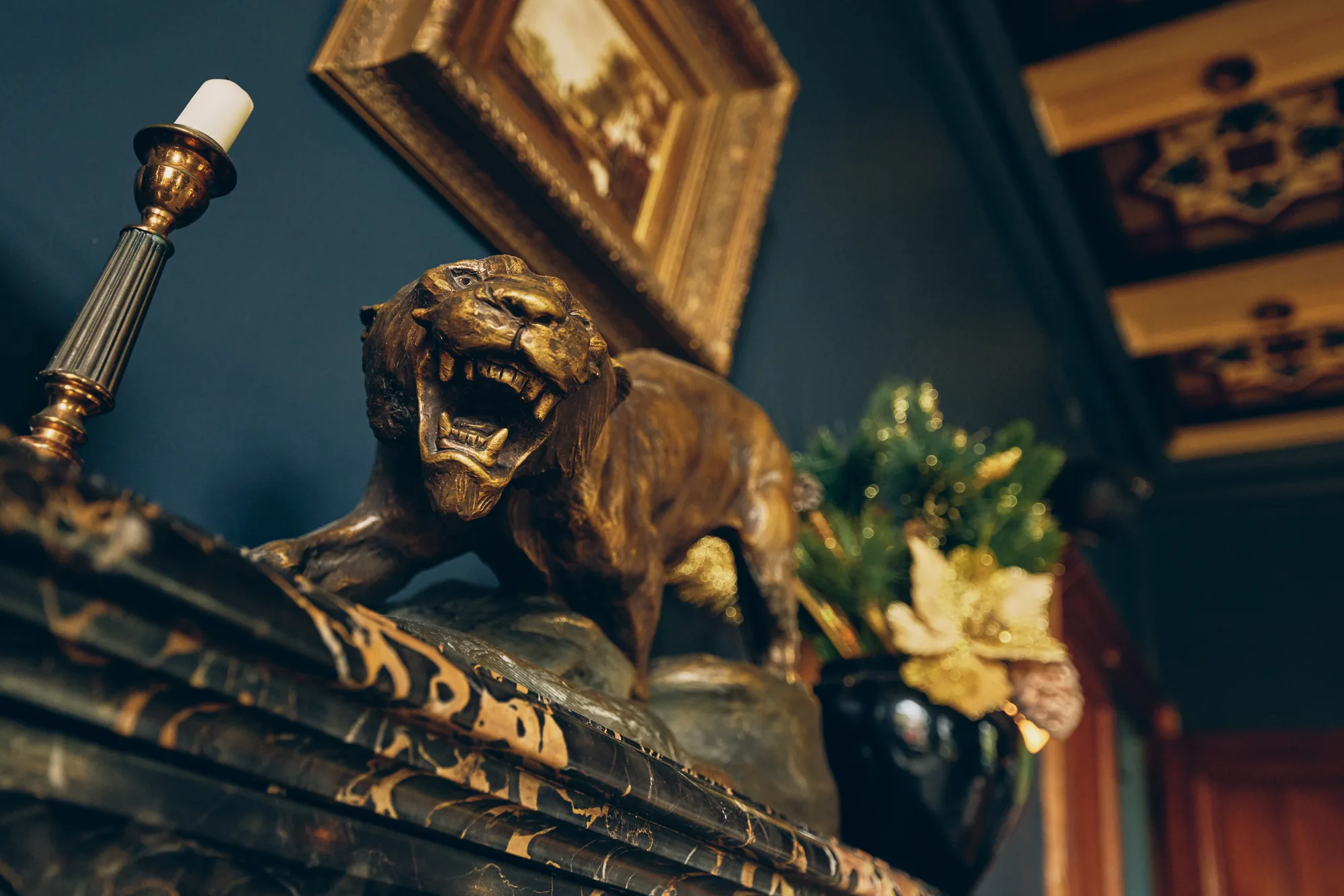 Sur la cheminée de marbre du bar, un tigre de bronze doré, une bougie et un tableau ancien