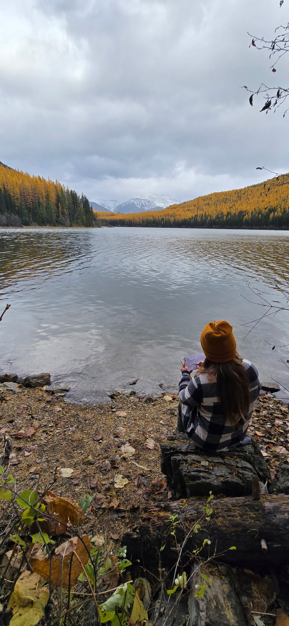 A person journaling beside an autumn lake, with mountains in the distance.
